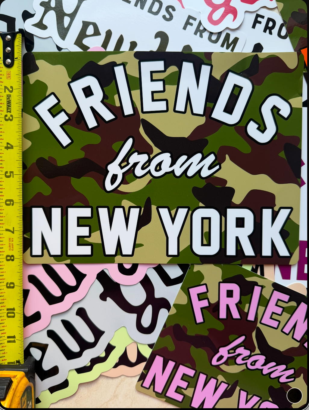 Oversized Friends From New York vinyl sticker in woodland camouflage with white lettering, shown beside a measuring tape.